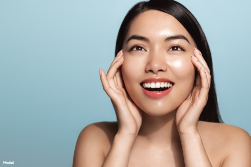 Joyful woman with glowing skin touching her face and smiling