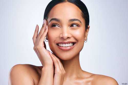 Joyful woman with clear, bright skin smiling and gently touching her temple